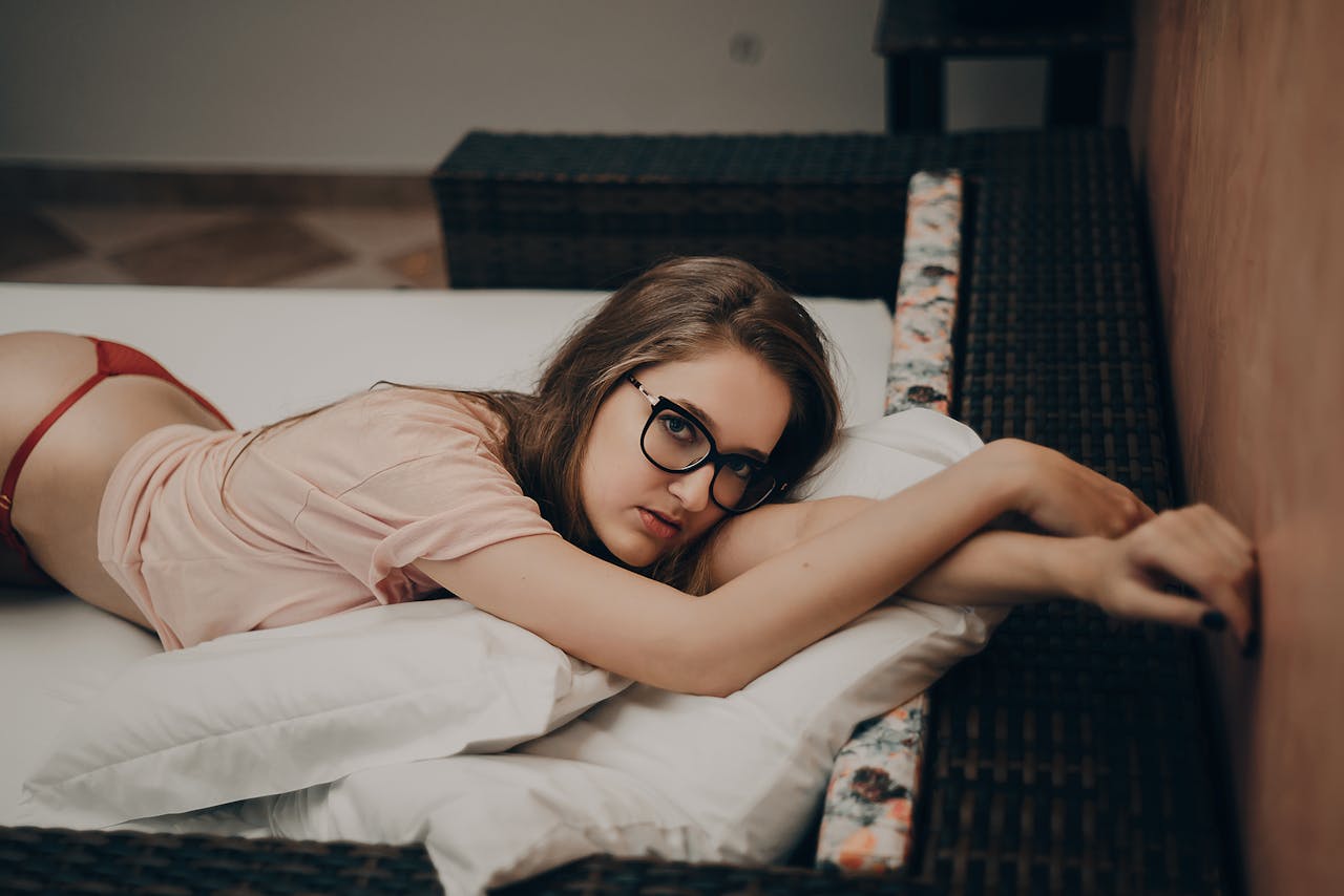 about-03 Young woman relaxing on a bed indoors, wearing glasses and casual attire.