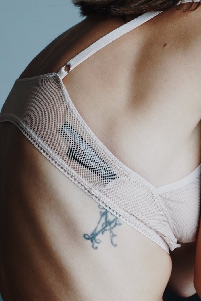 Intimate close-up of a woman's back with tattoo and mesh lingerie, exploring feminine identity.