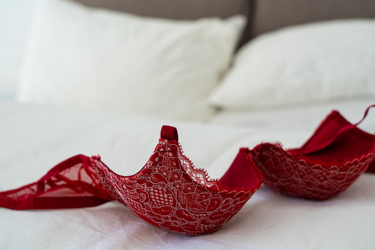 about-04 A red lace bra elegantly laid on a white bed in a stylish bedroom setting.