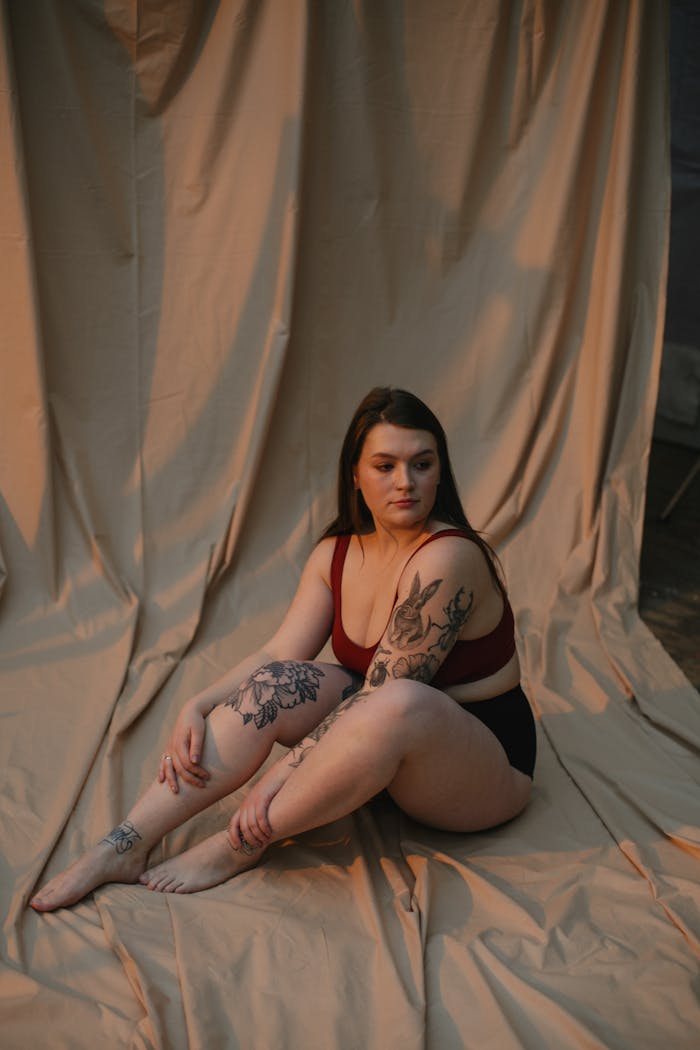 A tattooed woman posing thoughtfully against a curtain backdrop.