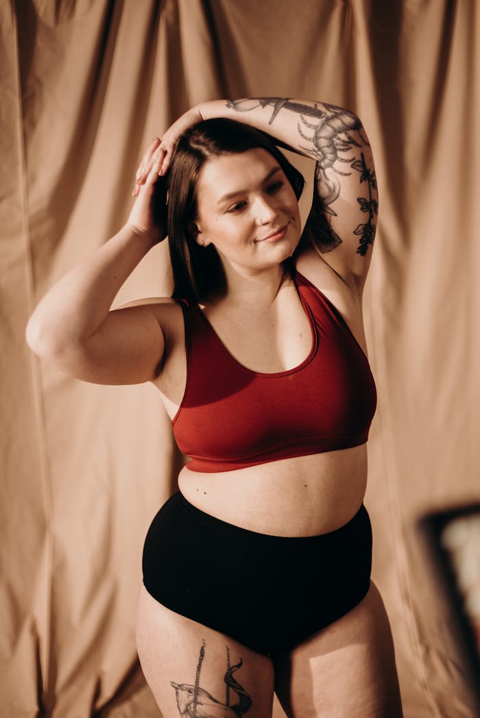 A confident plus size woman posing in lingerie, showcasing body positivity and beautiful tattoos.