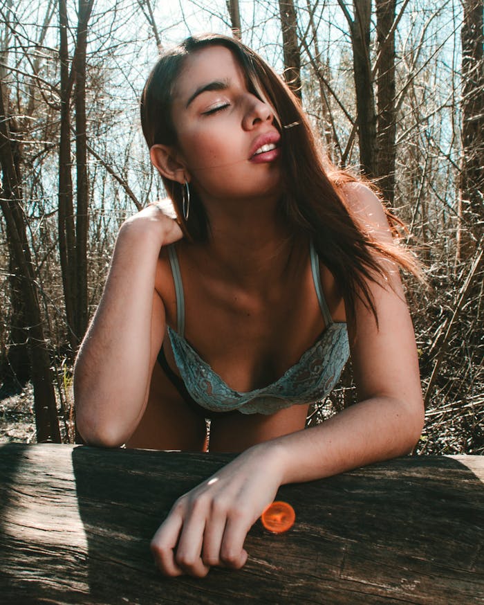 A young woman in lingerie poses confidently in a scenic forest setting, embracing nature.